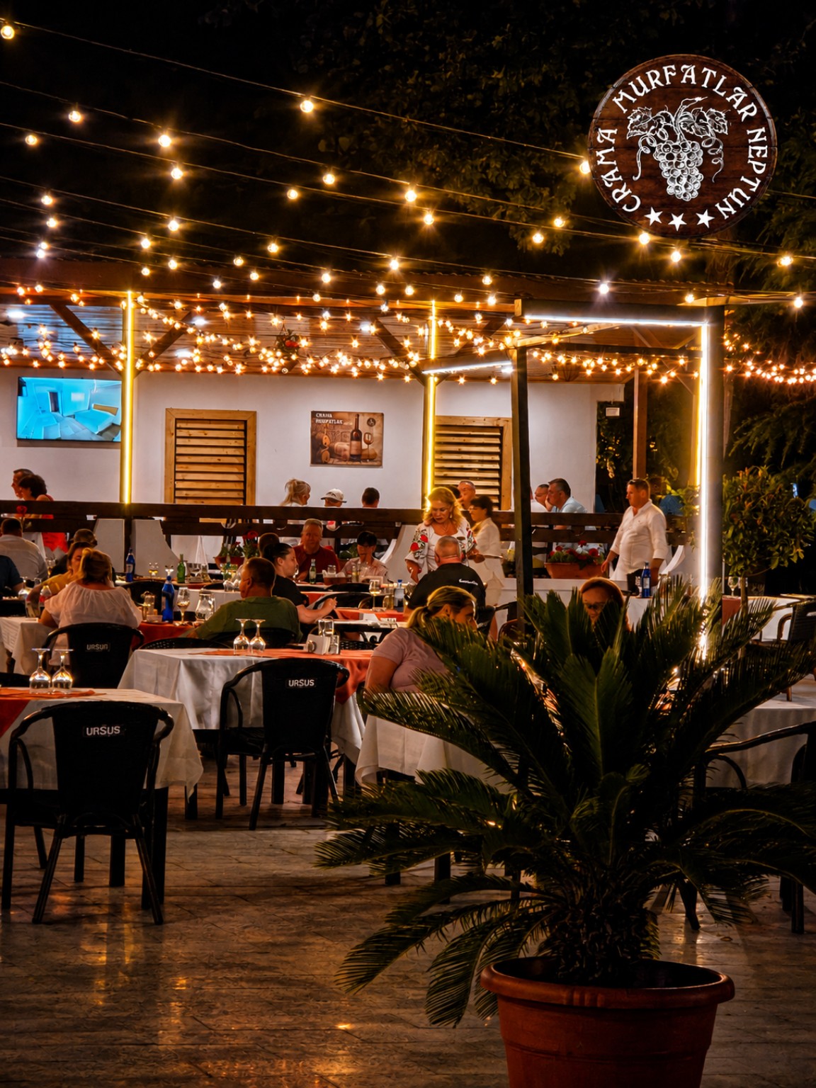 Terasa restaurantului seara, cu mese, lumini calde și plante